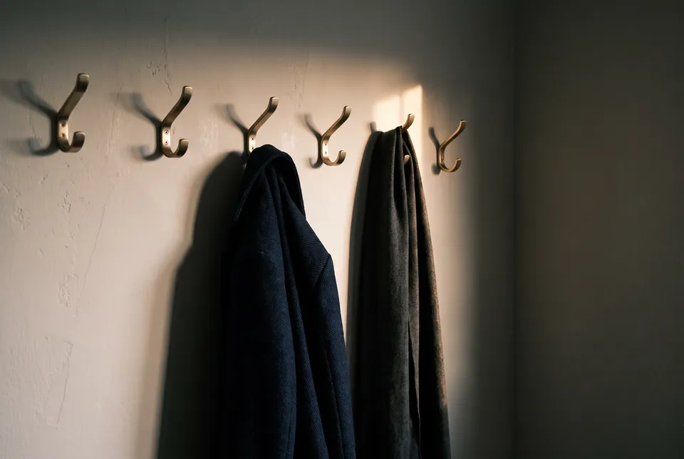 Manteau et écharpe à des patères de laiton, lumière du matin
